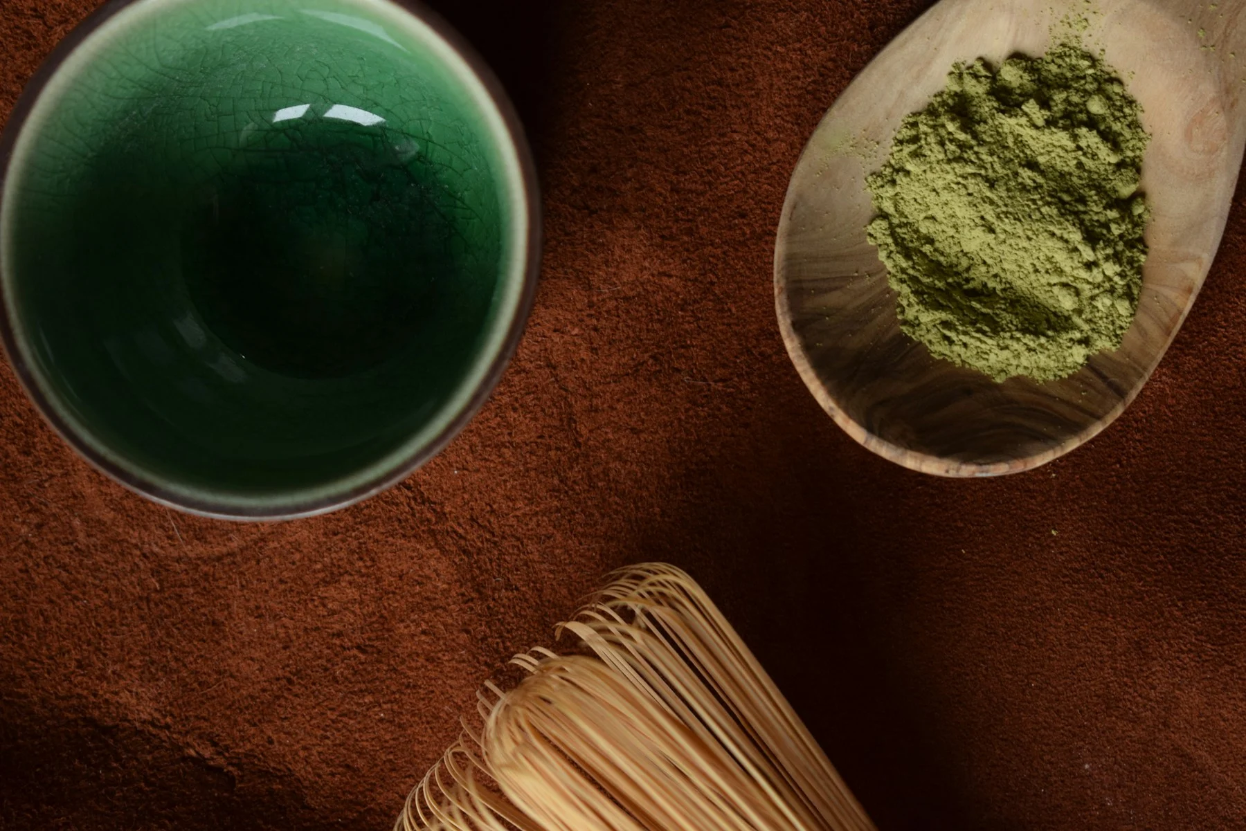Premium Japanese matcha powder in wooden spoon with bamboo whisk and ceramic bowl showing vibrant emerald green color